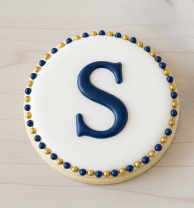 custom-sugar-cookies-melissa-tx-the-doodle-baker blue "S" with a navy and gold royal icing beaded border.