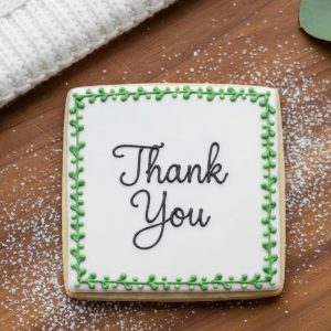 Thank You" sugar cookie with elegant black calligraphy and a green vine royal icing border.