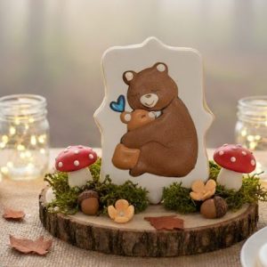 Rectangular scalloped sugar cookie with royal icing art of a brown mama bear hugging a baby bear with a blue heart.